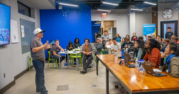 A student pitching to a panel of judges and a crowd of his peers